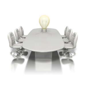 A conference table surrounded by six chairs has a light bulb morphing out of its center in this business clip art.
