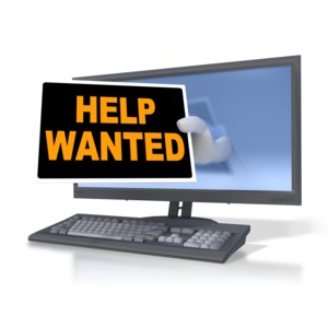 A hand hold out a help wanted sign from a computer monitor.  A concept of job hunting on-line or looking for work.