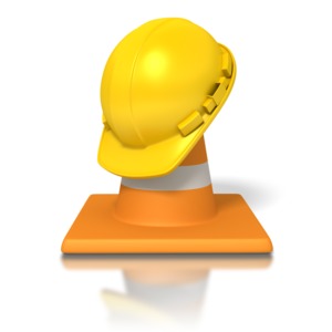 An image of a yellow hardhat on top of an orange traffic pylon.  A concept of construction or road work.
