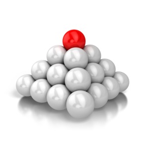 A single red ball sits on top of a pyramid shaped stack of metallic balls.  A concept of achievement, reaching a goal, or success.