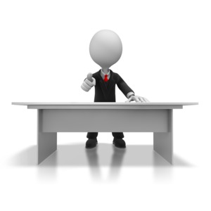 A boss or business person stands behind a desk and points at the viewer.  It could be used as a business call to action or a business warning.