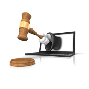 A courtroom judges arm holding a gavel emerges from a laptop computer screen.