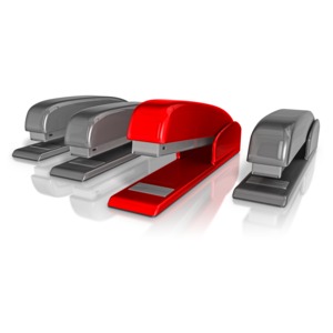 This clip art image shows four office staplers with a one standing out from the rest.