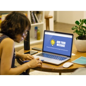 A young woman works at a table on a laptop computer. You may upload a screenshot or use our on-line tools to customize the message on the laptop.