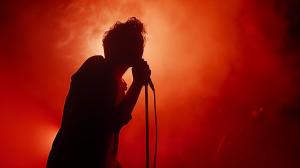 A silhouette of a singer performing against a vibrant red smoky background. 

