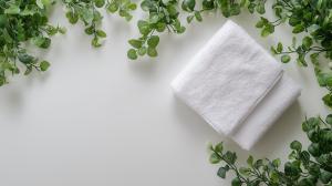 A white towel surrounded by green foliage on a light surface, evoking tranquility and cleanliness. 

