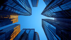 A low-angle view of skyscrapers reflecting light against a blue sky, showcasing modern architecture. 


