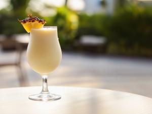 A refreshing cocktail with a pineapple garnish, set against a blurred tropical background. 

