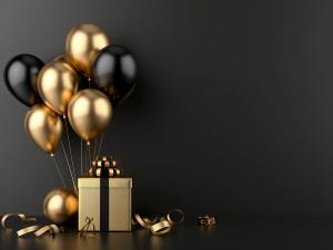 A festive arrangement of black and gold balloons with a gift box on a dark background. 

