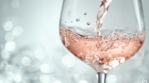 Sparkling rosé wine being poured into a glass with a blurred background.

