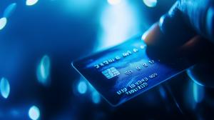 A close-up of a hand holding a credit card with a blue illuminated background.

