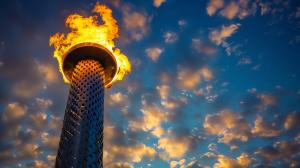 A modern tower with a flame against a dramatic sky, symbolizing energy and innovation.

