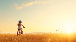 This image depicts a girl riding a bicycle in a golden field at sunset, symbolizing freedom and adventure.

