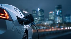 This image features an electric vehicle charging against a city skyline at night.


