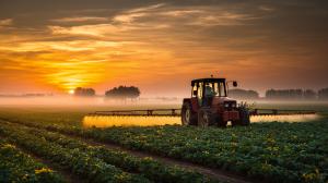 This image shows a tractor spraying crops at sunrise, symbolizing agriculture and farming practices.

