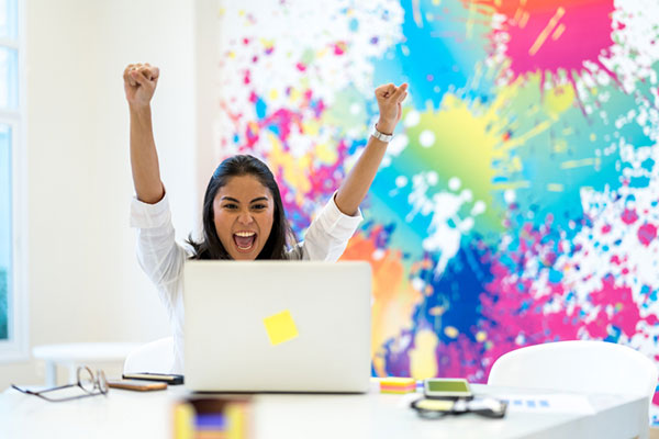 a woman with arms raised at laptop after creating a great and exciting presentation